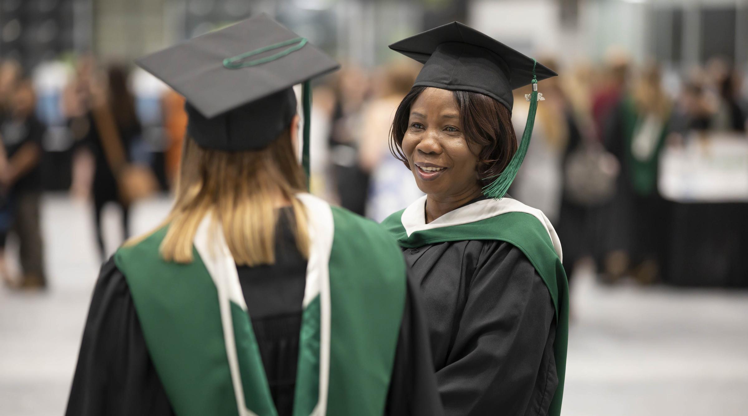 Two female students wearing convocation gowns in conversation