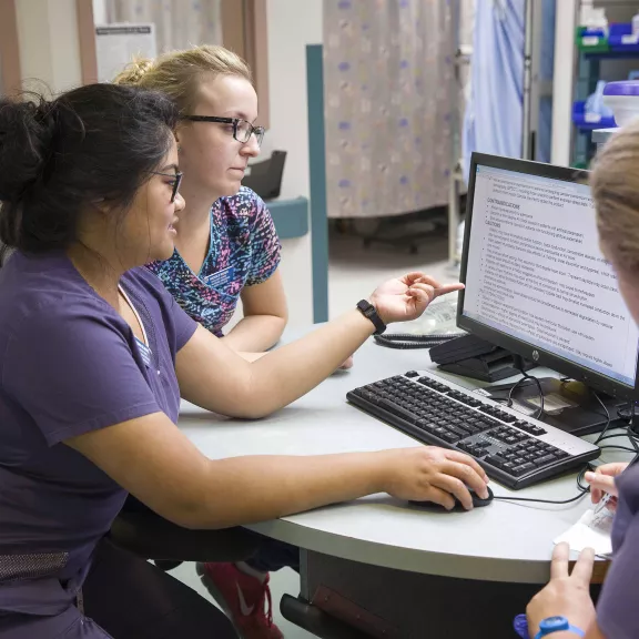 Three health care students on a computer in a hospital setting.