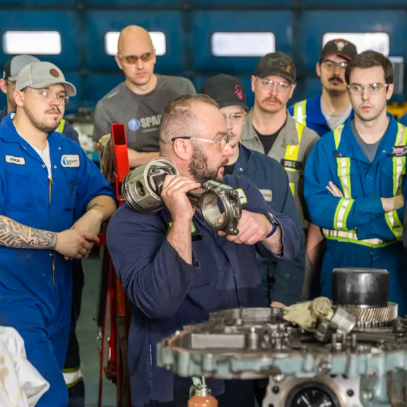 An instructor shows a group of students the inner workings of a large engine.