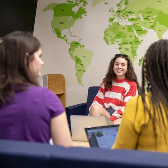 A group of female students smile and chat to each other in front of a map of the world